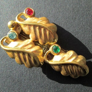 Peut inclure: Broche en forme de feuille dorée avec trois strass : un rouge et deux verts.