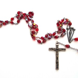 May include: A red glass bead rosary with a silver crucifix and a silver pendant featuring a figure of the Virgin Mary.