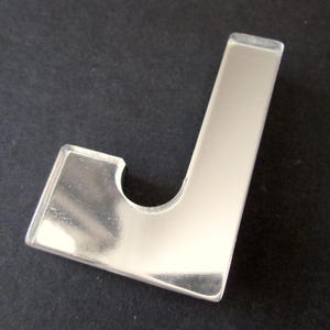 May include: A polished, silver-coloured metal hook, J-shaped with a curved cutout. The hook has a smooth, reflective surface. It is likely designed for hanging items.