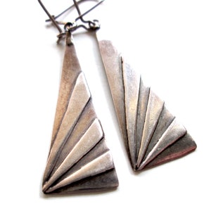 Peut inclure: Une paire de boucles d'oreilles en argent avec un motif géométrique. Les boucles d'oreilles sont en forme de triangles avec un motif en éventail.