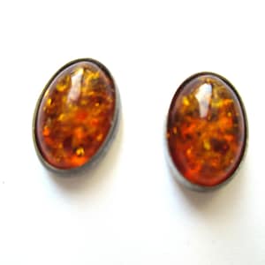 May include: A pair of oval-shaped amber earrings with silver settings. The amber is a warm, honey colour with flecks of gold throughout.