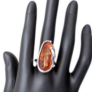 May include: A silver ring featuring a large, oval amber stone set in a delicate, swirling design.