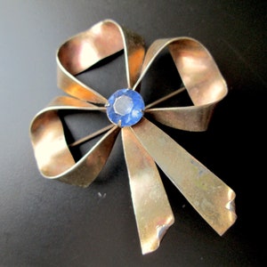 May include: A gold-toned metal bow brooch with a blue rhinestone in the centre.