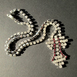 May include: A silver chain necklace with a large, red and clear rhinestone cross pendant.
