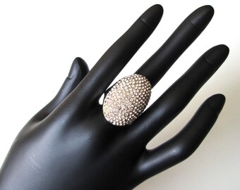 Puede incluir: Un anillo ovalado grande con un engaste plateado y un racimo de diamantes de imitación transparentes.