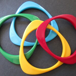 Peut inclure: Quatre bracelets colorés et entrelacés, bleus, verts, jaunes et rouges. Les bracelets lisses et incurvés sont en matériau brillant et sont disposés dans un motif visuellement attrayant. Ces accessoires sont un ajout vibrant à toute collection de bijoux.