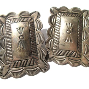 May include: A pair of vintage silver-toned earrings. Each earring features a rectangular centre with a decorative design and a scalloped edge. The earrings have a detailed, aged appearance.