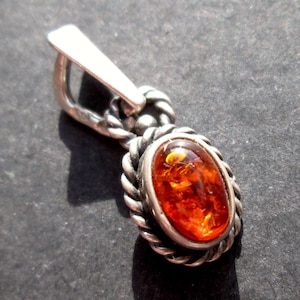 May include: A silver pendant with a rope-like design around an oval amber stone.