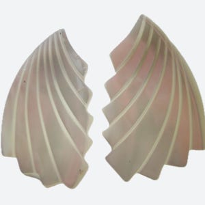 May include: Two abstract, fan-shaped objects with a layered design. The objects have a pale pink and white colour scheme, with curved, vertical lines creating a textured effect. The overall shape is reminiscent of a stylized wing or shell.