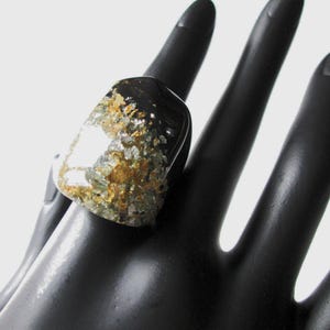 Peut inclure: Une bague noire avec un incrustation de résine transparente contenant des paillettes dorées et vertes.