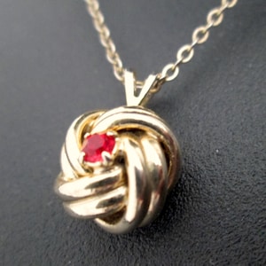 以下が含まれることがあります： 赤い宝石が結ばれたペンダントの付いたゴールドネックレス