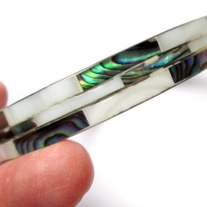 May include: A silver bangle bracelet with a white and iridescent abalone shell inlay. The bracelet has a geometric pattern.