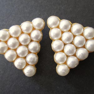 May include: A pair of gold tone earrings with a triangular shape. Each earring is made up of small, white faux pearls.