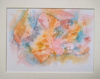 May include: Watercolour painting of leaves in shades of orange, pink, and blue. The leaves have intricate vein details and are set against a soft, blended background. The artwork is framed in a white mount.