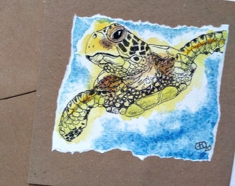 May include: A watercolor painting of a sea turtle on a square card. The turtle is depicted in shades of yellow, brown, and black, with a blue and yellow background. The card is set against a brown envelope.