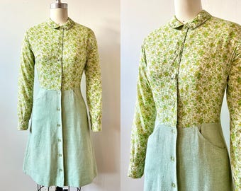 May include: A vintage-style dress with a floral print top and a solid, button-down skirt. The long-sleeved top features a pattern of small green flowers on a cream background. The skirt is a light green color with two pockets.