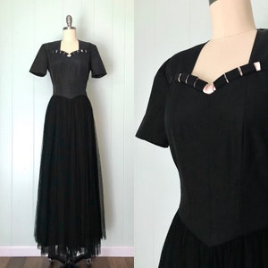 May include: A black vintage formal gown with a tulle skirt and a fitted bodice. The bodice has a sweetheart neckline and a decorative detail of silver-toned metal accents.
