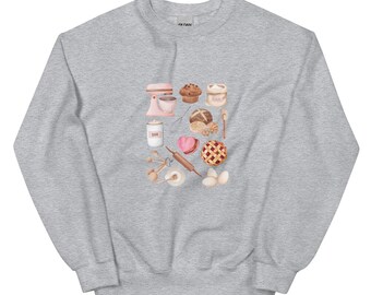 May include: A light gray sweatshirt featuring a watercolor illustration of baking tools and treats. The design includes a pink stand mixer, muffins, a flour bag, measuring spoons, a rolling pin, and a pie. The word "SUGAR" is visible on a jar.