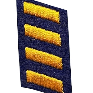 May include: A dark blue fabric patch with four gold stripes sewn on. The patch is shaped like a chevron.