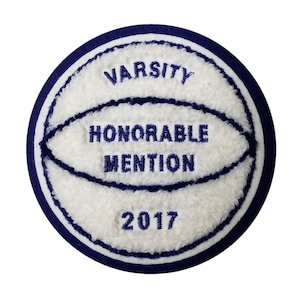 May include: A round, white and blue varsity patch with the words "VARSITY HONORABLE MENTION 2017" embroidered in navy blue. The patch has a basketball design and a navy blue border.
