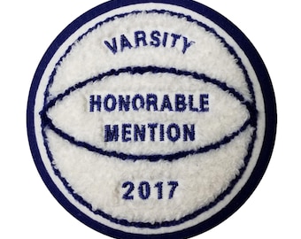 May include: A round, white and blue varsity patch with the words "VARSITY HONORABLE MENTION 2017" embroidered in navy blue. The patch has a basketball design and a navy blue border.