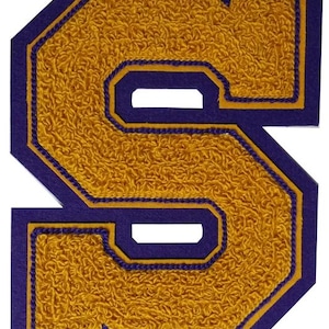 May include: A large, gold felt letter "S" with a purple outline. The letter is in a varsity style font and is perfect for adding a personalized touch to clothing, bags, or other items.