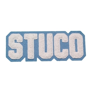 Può includere: Un toppa di feltro blu con la parola "STUCO" in lettere di feltro bianco.