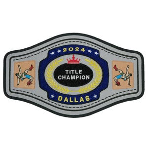 May include: A silver wrestling championship belt with blue and yellow accents. The belt features the text "2024 TITLE CHAMPION DALLAS" and a wrestler in a pin.
