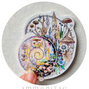 May include: A colorful, circular sticker featuring a fantasy illustration with mushrooms, flowers, and a castle. The sticker has the text "MYTHOS AND ALCHEMY" at the top and "AMMONITAE" and "WEATHERPROOF STICKER" at the bottom.