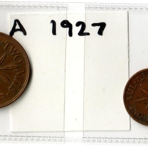 May include: Two vintage bronze coins, one larger and one smaller, displayed in a clear plastic holder. The larger coin has text and a sprig design. The smaller coin also has text and a sprig design. The year "1927" is written above the coins.
