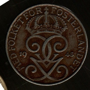 May include: A close-up of a vintage coin with the text "MED FOLKET FOR FOSTERLANDET" and the years 1945 and 1919. The coin has a crown design and ornate lettering. The coin is a bronze color.