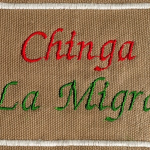 May include: A brown canvas patch with white stitching around the edges. The words "Chinga La Migra" are embroidered in red and green thread.