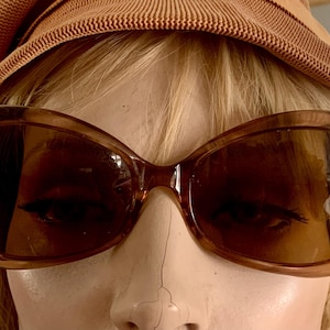 Peut inclure: Lunettes de soleil marron surdimensionnées avec un chapeau marron assorti. Les lunettes ont une monture épaisse et des verres teintés. Le chapeau est de couleur marron clair et a un aspect texturé. Les lunettes et le chapeau sont probablement vintage.
