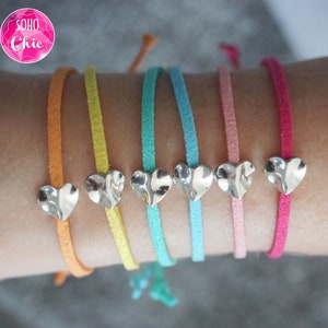 Puede incluir: Seis pulseras de ante de colores vivos con abalorios de corazón plateados. Las pulseras son naranja, amarilla, turquesa, azul claro, rosa y roja.