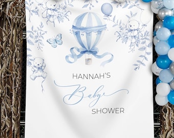 May include: White baby shower banner with blue watercolor illustrations of a hot air balloon, teddy bears, and butterflies. The banner reads "HANNAH'S Baby Shower" in elegant script. Balloons in shades of blue and white decorate the top.