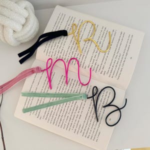 May include: Four wire bookmarks in different colors, pink, gold, black, and green, with velvet ribbon tassels. The bookmarks are shaped like the letters R, M, U, and B.