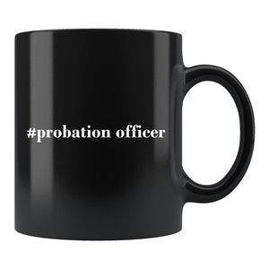 May include: Black ceramic mug with a white handle. The mug features the text "#probation officer" in a white, sans-serif font. The mug is a standard size and shape, suitable for hot or cold beverages.
