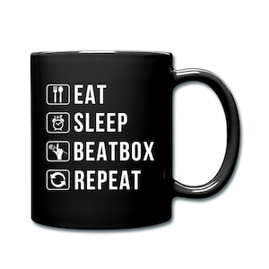 May include: Black ceramic mug with a white graphic. The graphic includes icons of a fork and knife, alarm clock, microphone, and a circular arrow, with the words "EAT SLEEP BEATBOX REPEAT" in a bold, sans-serif font. The mug has a curved handle.