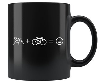 May include: Black ceramic coffee mug with a white graphic of mountains, a bicycle, an equals sign, and a smiley face. The text reads "Mountains + Bicycle = Happy".