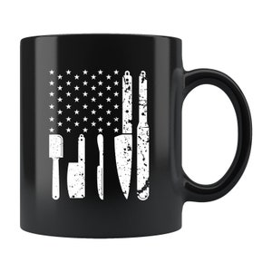 May include: Black ceramic coffee mug with a white design of a US flag made of kitchen knives and a spatula.