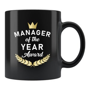 May include: Black ceramic mug with a white inscription that reads "Manager of the Year Award" with a gold crown and laurel wreath.