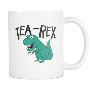May include: White ceramic mug with a green cartoon dinosaur holding a cup of tea. The text "TEA-REX" is printed in black above the dinosaur.