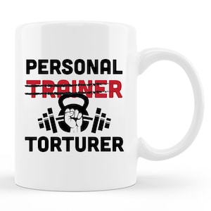 May include: White ceramic mug with the words "PERSONAL TRAINER" crossed out in red, replaced by "TORTURER" in black. A black graphic of a kettlebell and barbell is centered below the text. The mug has a white handle.