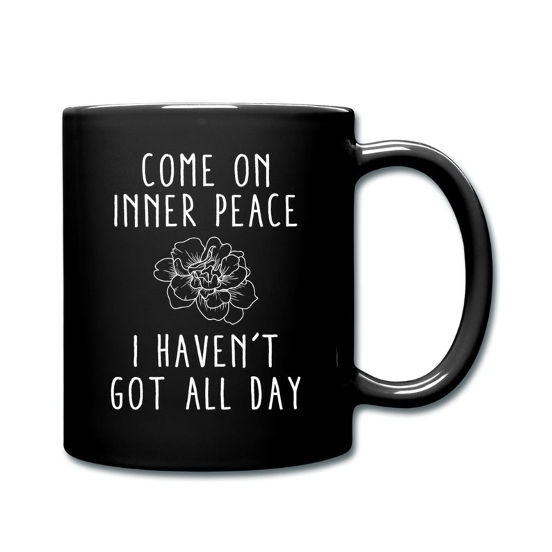 May include: Black coffee mug with white text that reads "Come on inner peace I haven't got all day". A stylized flower is between the two lines of text.
