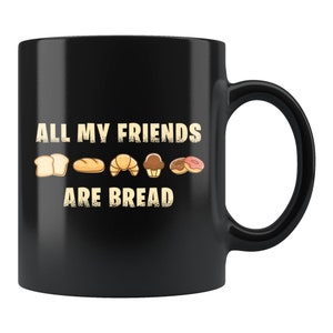 May include: Black coffee mug with white text that reads "All my friends are bread" and a row of bread-related icons including a loaf of bread, a baguette, a croissant, a muffin, and a donut.