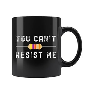 May include: Black ceramic coffee mug with the text "YOU CAN'T RESIST ME" in white, featuring a colorful resistor graphic. The mug has a large handle and a glossy finish, perfect for a tech enthusiast.