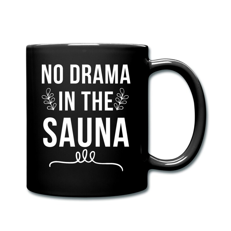K&ouml;nnte beinhalten: Schwarze Kaffeetasse mit wei&szlig;em Text, der "No Drama in the Sauna" lautet, mit einer dekorativen Verzierung darunter.