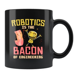 May include: Black coffee mug with a white design that says "Robotics is the bacon of engineering". The design includes a cartoon robot and a piece of bacon.