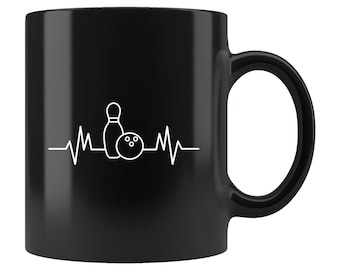 May include: Black ceramic coffee mug with a white outline of a bowling pin and ball with a heartbeat graphic. The mug has a white handle.