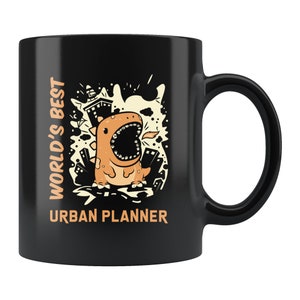 May include: Black coffee mug with a graphic of a cartoon dinosaur with its mouth open, surrounded by city buildings. The text "WORLD'S BEST URBAN PLANNER" is printed on the mug.
